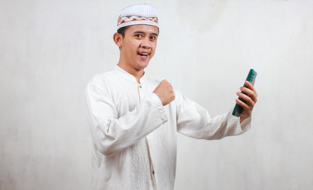 Portrait of young Asian muslim man using mobile phone against white background