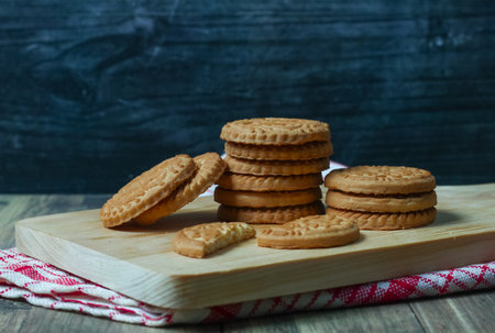 Sandwich cookies on a cutting board on a dark wooden background.