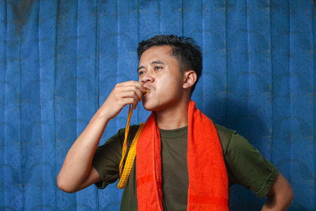 Young Asian man eating a carrot with orange towel around his neck.