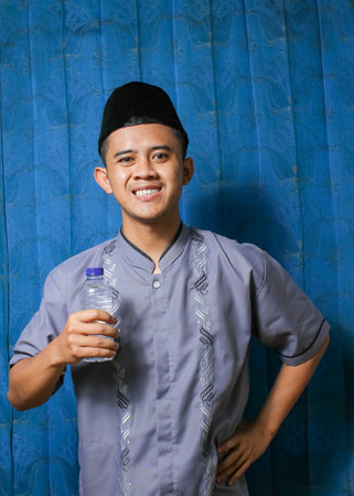 Portrait of young asian muslim man holding water bottle.