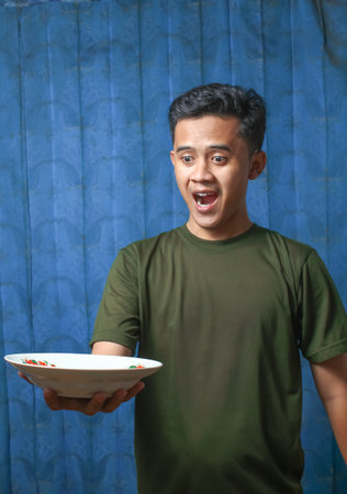 Young Asian man holding a plate of food on a blue background.