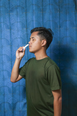 Young Asian man holding a thermometer in his hand against a blue curtain