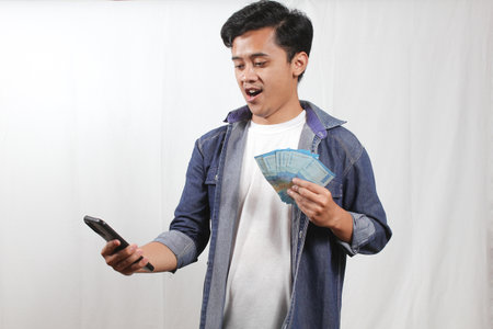 asian young man using mobile phone and holding money on white background