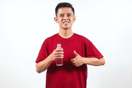 Young Asian man holding a bottle of water and thumbs up on white backgroundの写真素材