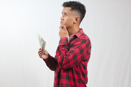 Young asian man thinking and looking at money on white background.の写真素材