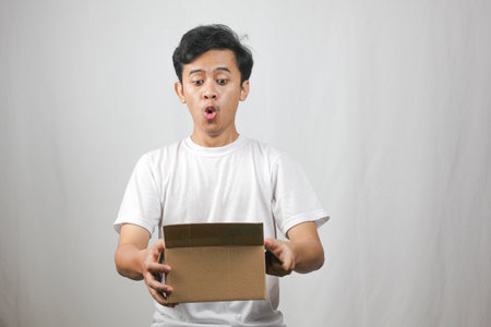 Excited young man opening a package with a surprised expression, perfect for illustrating online shopping excitement and delivery services joy in a modern wayの写真素材