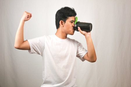 Young asian man drinking from a plastic bottle on white backgroundの写真素材