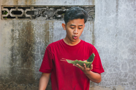 Asian man surprised and happy holding traditional dish of chicken satay and lontong wrapped in...