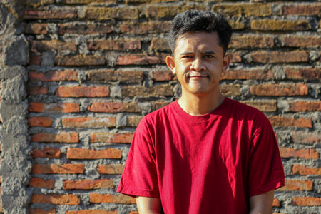 Asian man smiling face exposed to morning sunlight with brick wall backgroundの写真素材