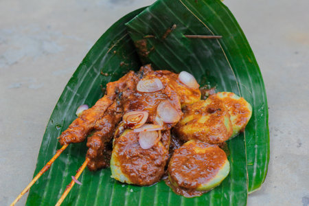 traditional Indonesian food, chicken satay and lontong sprinkled with peanut sauce and sliced ââshallots wrapped in banana leavesの写真素材