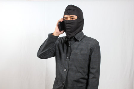 Asian man wearing a black balaclava talking on the phone.の写真素材
