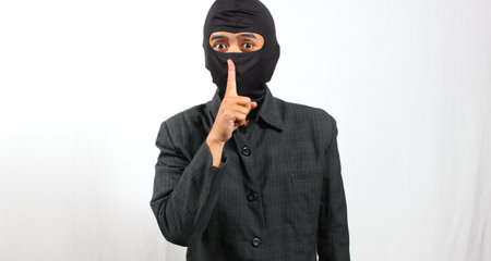 Young asian man wearing balaclava and black suit pointing at somethingの写真素材