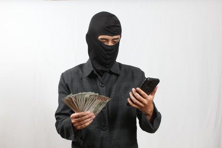 man in balaclava holding mobile phone and money on white background