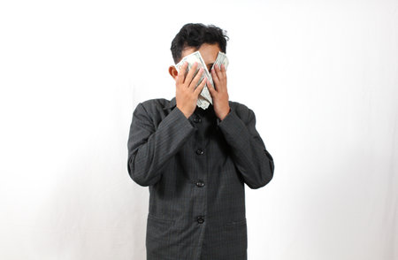 Asian businessman covering his face with money. Isolated on white background.の写真素材