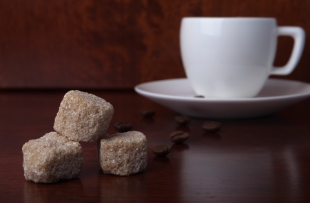 Pieces of brown sugar on wooden table with coffe beans and white cupの写真素材