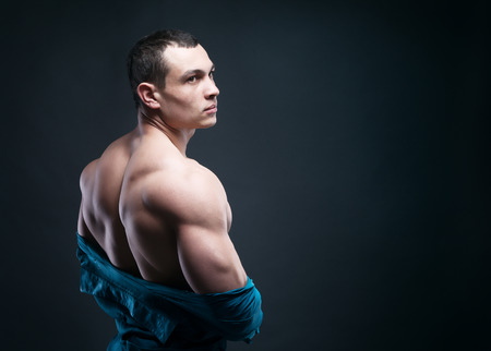 muscular athletic guy takes off his shirt on a dark backgroundの写真素材