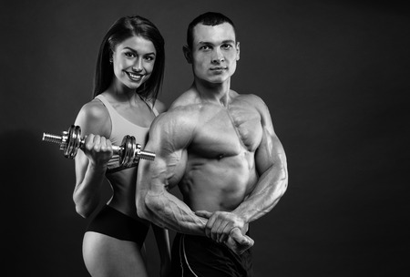 Athletic man and woman with a dumbells on dark backgroundの写真素材
