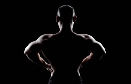 Bodybuilder demonstrates latissimus dorsi on a dark background is over contrast.  Confident young fitness  athlete man. Back view.の写真素材