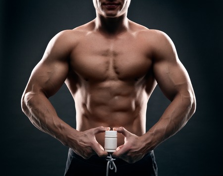 Close up of muscular man torso with hand full of pills. Concept of drugs, doping, anabolic steroids in sports.の写真素材
