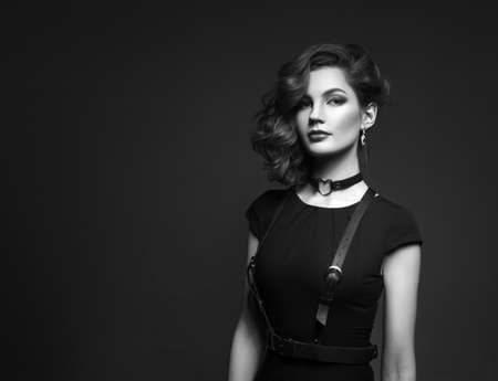 Portrait of beautiful woman with red hair and elegant hairstyle in black dress posing on gray background in studio. Fashion photo.の写真素材