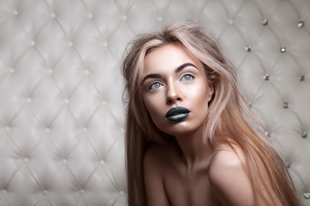 Studio portrait of a sexy blond, over leather upholstery background. Elegant luxury woman with a seductive neckline and bare shoulders looks into the camera.の写真素材