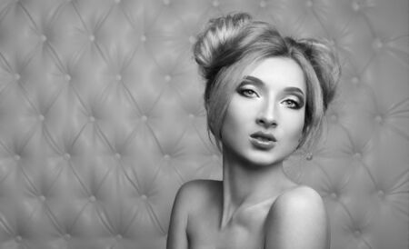 Studio portrait of a sexy blond, over leather upholstery background. Elegant luxury woman with a seductive neckline and bare shoulders looks into the camera.の写真素材