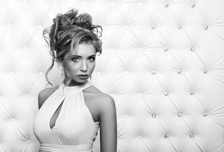 Studio portrait of a sexy blond in dress, over leather upholstery background. Elegant luxury woman with a seductive neckline and bare shoulders looks into the camera.の写真素材