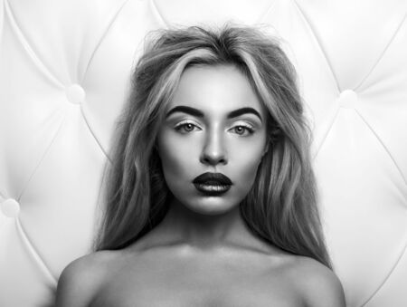 Studio portrait of a sexy blond, over leather upholstery background. Elegant luxury woman with a seductive neckline and bare shoulders looks into the camera. Black and white photo.の写真素材