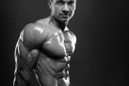 Strong bodybuilder with six pack. Athlete man with perfect abs, shoulders,biceps, triceps and chest, personal fitness trainer flexing his musclesの写真素材