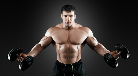 Portrait of bodybuilder with dumbbells in his arms on grey background in a studio. Isolated with clipping path.の写真素材