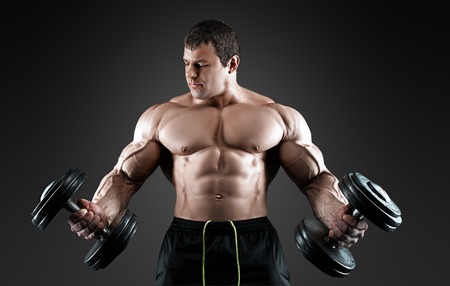 Portrait of bodybuilder with dumbbells in his arms on grey background in a studio. Isolated with clipping path.の写真素材