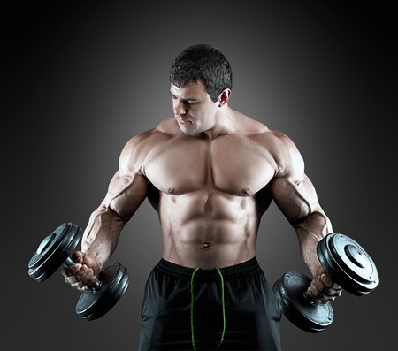 Portrait of bodybuilder with dumbbells in his arms on grey background in a studio. Isolated with clipping path.の写真素材