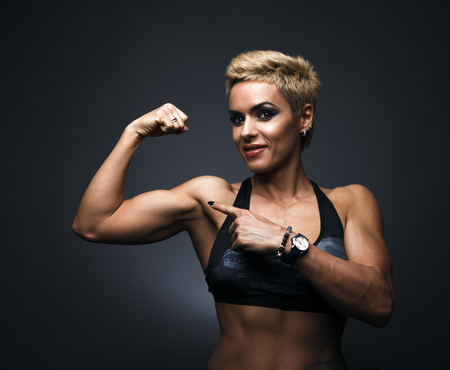 Cheerfully smiling sporty woman demonstrating bicepsの写真素材