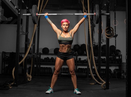 Full length portrait of muscular woman in a gym doing heavy weight exercises