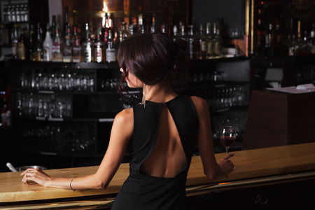 beautiful young brunette woman in black dress with glass of red wine in her handの写真素材