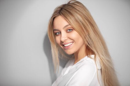 Portrait of a smiling blonde in a white blouse on a light background.の写真素材