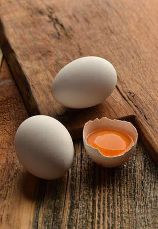 Chicken eggs and half broken egg with yolk on wooden backgroundの写真素材