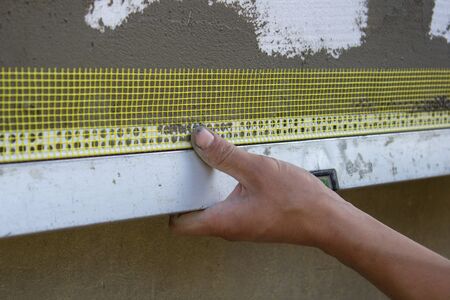 builder's hand glues on the facade of the corner with a grid on the house