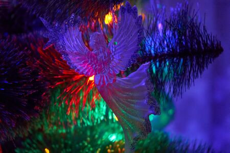 Christmas angel at night hanging on a Christmas tree glowing in colorful garlandsの写真素材