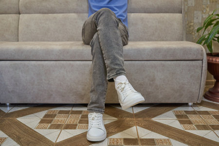 young man sitting on the sofa, student in the office, legs of the guy sitting on the sofaの写真素材