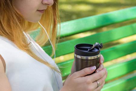Young woman listening to music and drinking coffee in the parkの写真素材