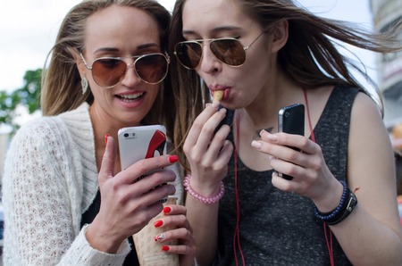 Two girlfriends are using cellphone on the streetの写真素材