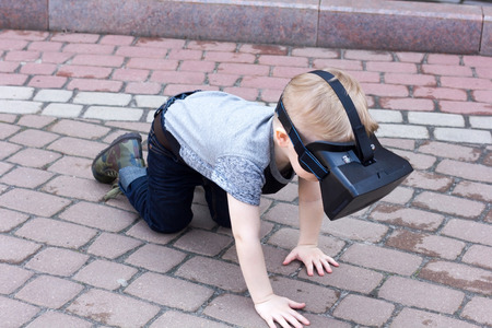 Boy in t-shirt and jeans with the virtual glasses is crawling