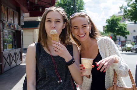 Two girlfriends are eating icecream and drinking coffee on the stretの写真素材