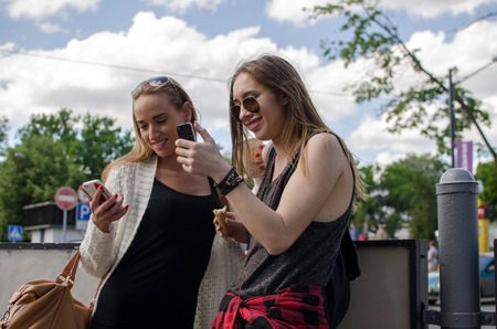 Two girlfriends are using phones on the street