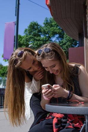 Two girlfriends are using cellphone in the cafeの写真素材