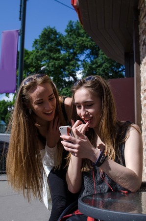 Two girlfriends are using cellphone in the cafeの写真素材
