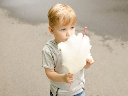 Small baby boy is eating cotton candy in the park