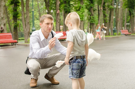 Small baby boy is eating cotton candy in the park with his fatherの写真素材
