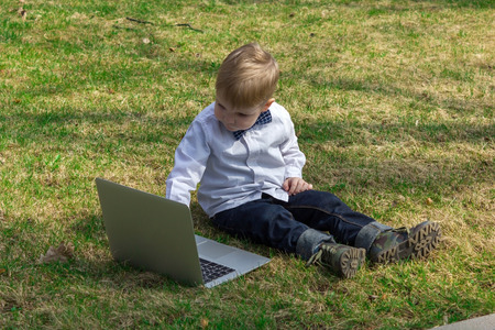 Small boy sitting on the green grass and typing on silver laptopの写真素材